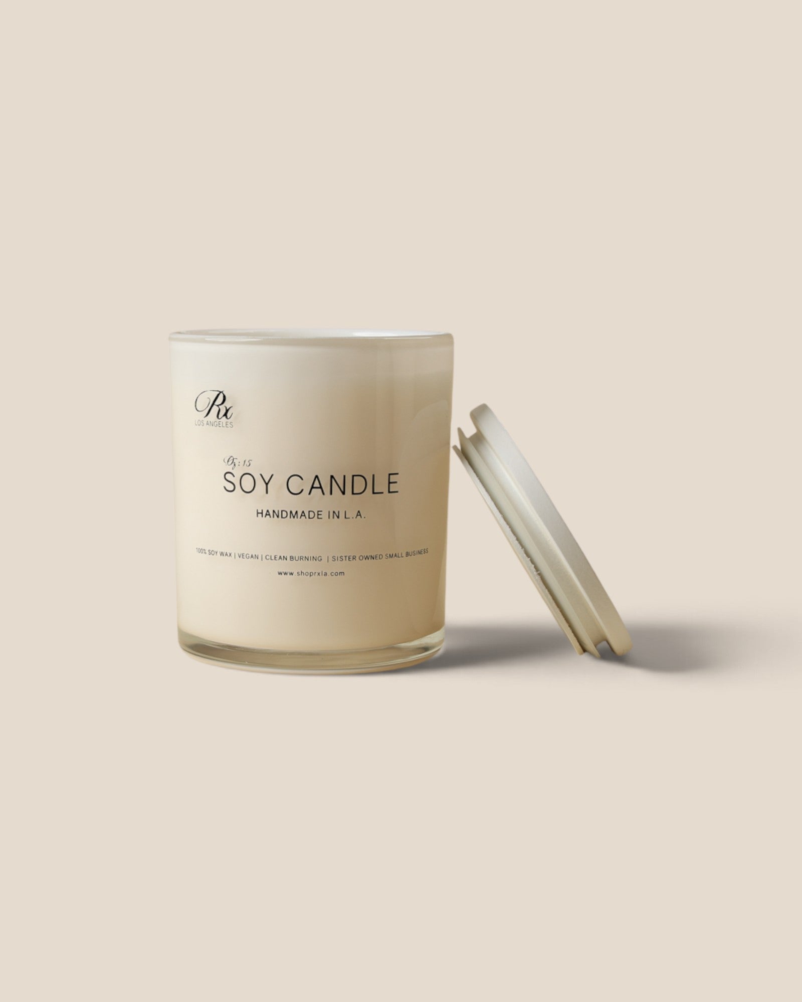 A minimalist soy candle in a clear glass jar with a cream-colored wax and a matching lid leaning against it, set against a solid beige background.