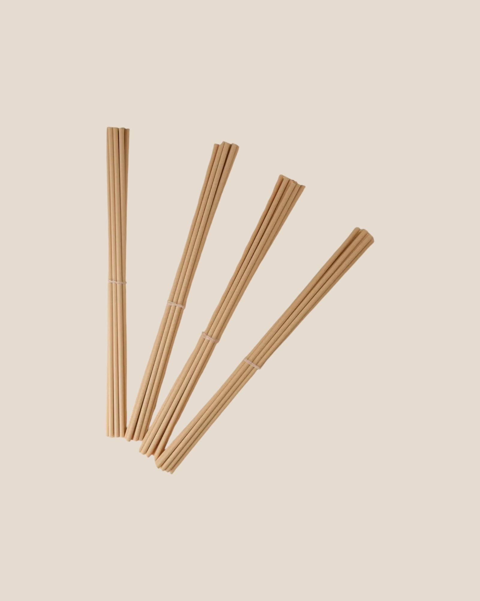 Four bundled fiber diffuser reeds in a fan shape on a solid beige background.