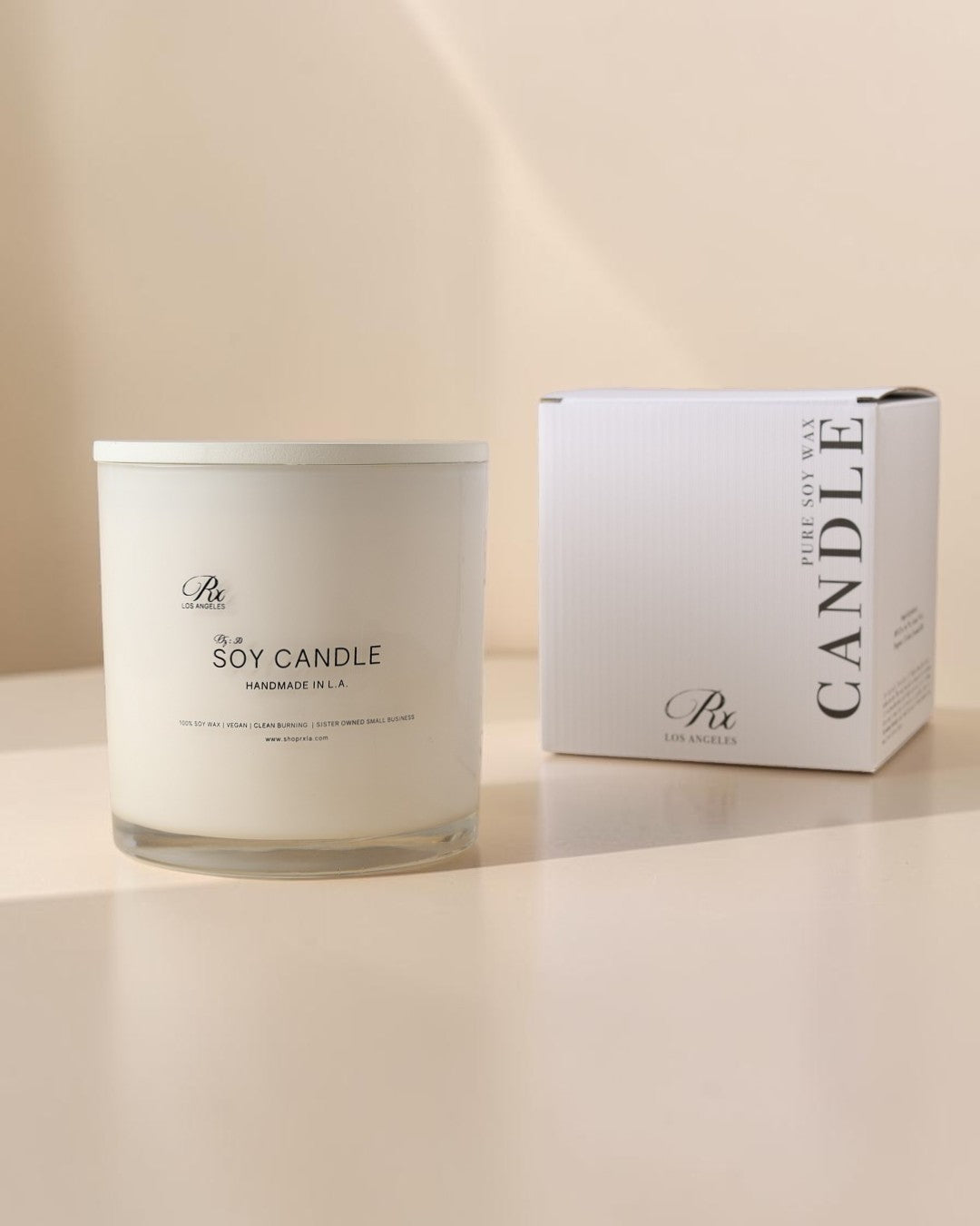 A white soy candle in a clear glass jar sits beside its white packaging box on a warm beige surface. The labels show the brand 'B&H' and the scent name 'Embrace of Nature'.