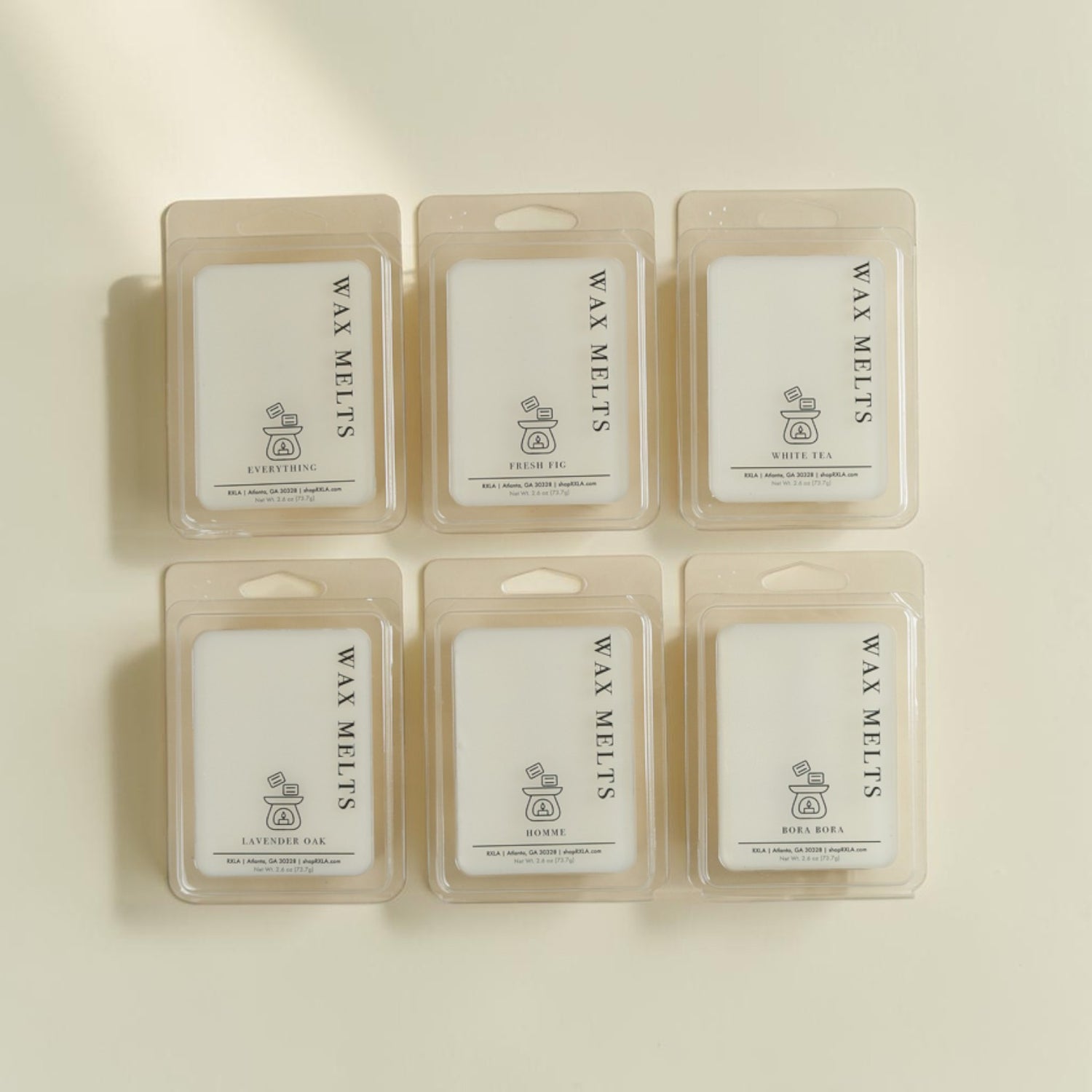 Six wax melts in clear plastic clamshell packages arranged in two rows on a warm off-white background. Each package contains a white wax melt card with the text 'WAX MELTS' and 'EVERYDAY' printed vertically, plus a small logo.