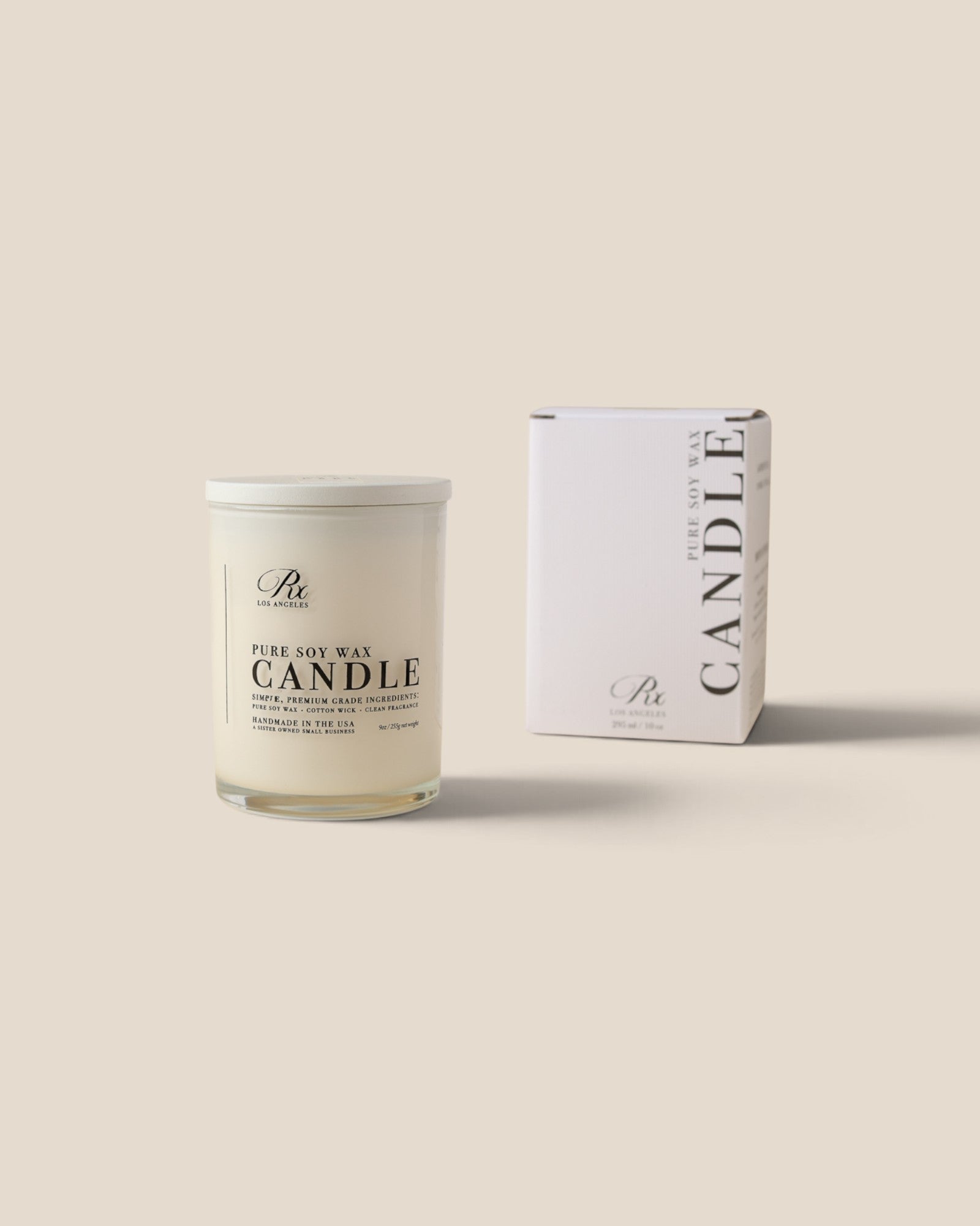 A white soy wax candle in a clear glass jar with a white lid, shown next to its white packaging box on a solid beige background. The brand logo 'RXLA is visible on both the candle label and the box.