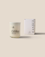 A white soy wax candle in a clear glass jar with a white lid, shown next to its white packaging box on a solid beige background. The brand logo 'Rt' is visible on both the candle label and the box.