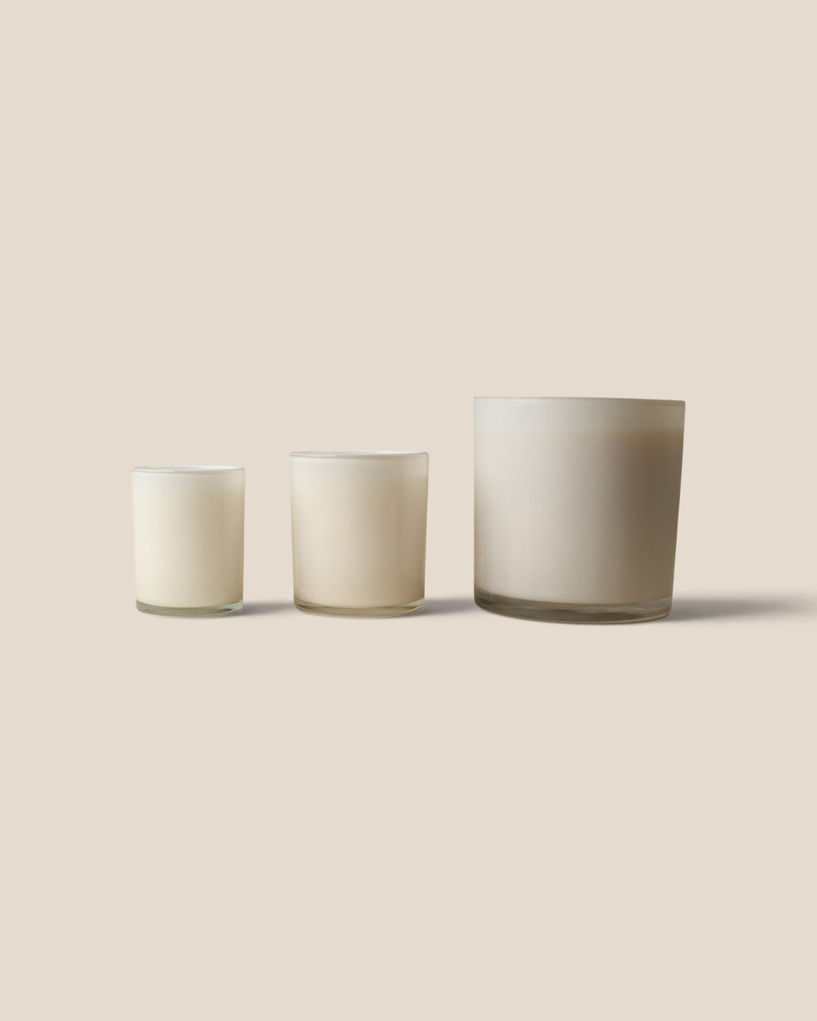 Three frosted glass candle holders in different sizes arranged in ascending order of height against a solid beige background.