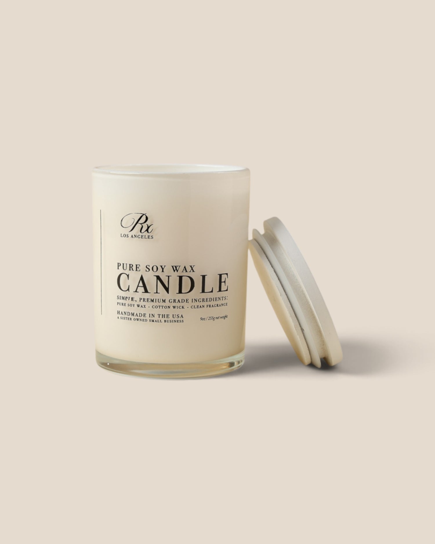 A clear glass jar candle filled with creamy off-white wax, shown with its matching lid leaning against it on a warm beige background. The front label reads 'Rx Los Angeles' and 'PURE SOY WAX CANDLE'.