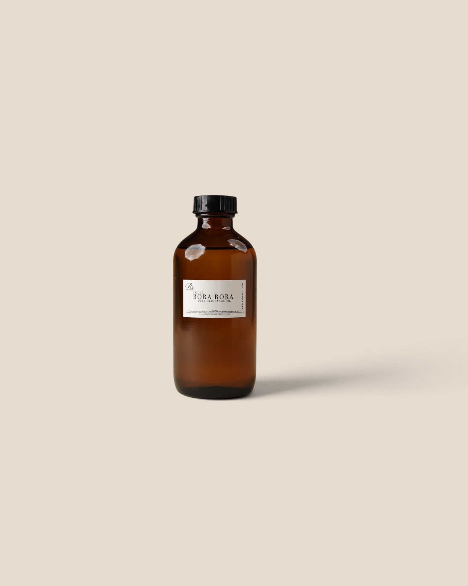 An amber glass bottle with a black cap and a white label reading 'Bora Bora', centered against a solid beige background.