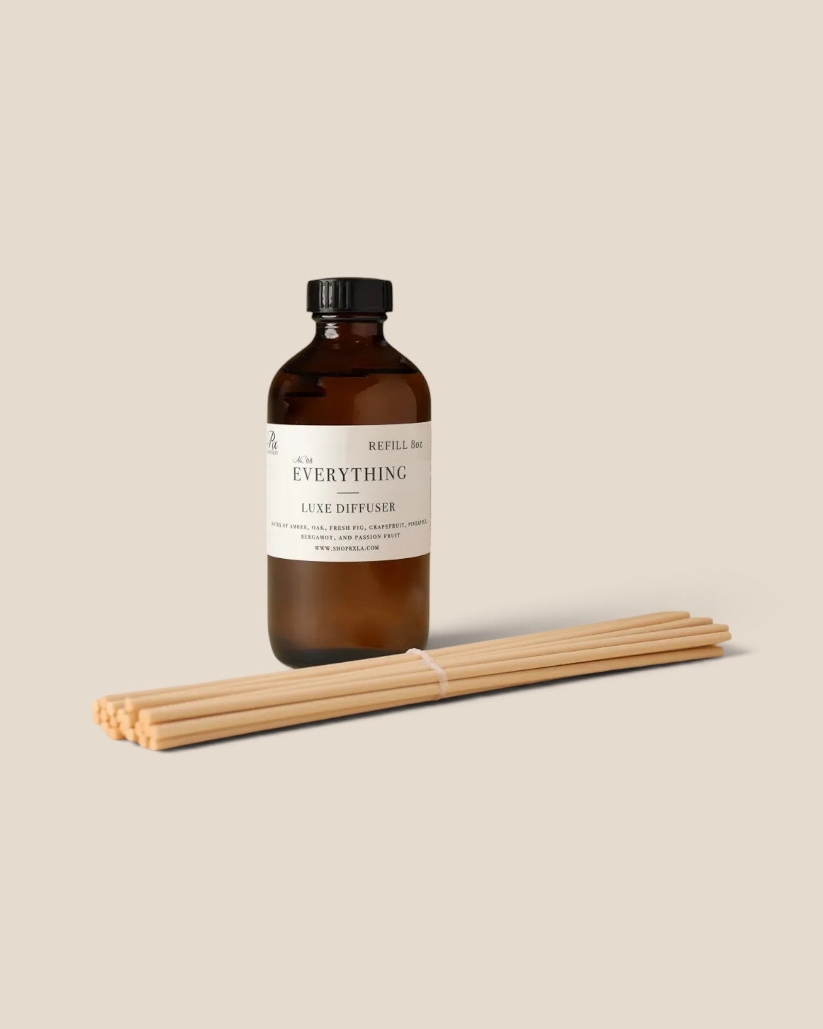 An amber glass reed diffuser bottle with a white label reading 'The Everything Reed Diffuser' and a bundle of natural reed sticks placed in front, on a warm beige background.