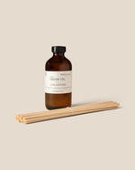 An amber glass diffuser bottle with a black cap and a cream label reading 'FRESH FIG' and 'LANE DIFFUSERS,' shown with a bundle of natural wood wicks on a warm beige background.