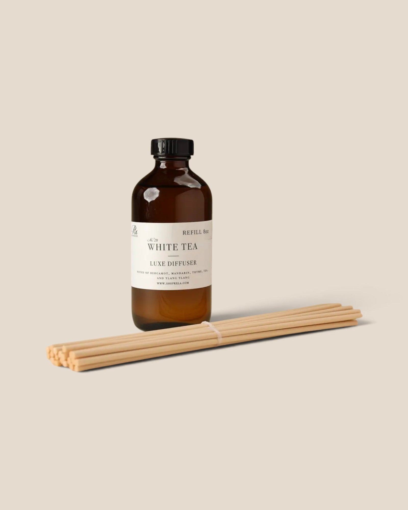 An amber glass bottle of luxury diffuser with a cream label reading 'THE WHITE TEA' and 'LUXE DIFFUSER', shown with a bundle of diffuser fiber reed sticks on a solid beige background.