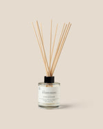 A reed diffuser bottle  filled with clear liquid and topped with fiber reeds, centered on a warm beige background.