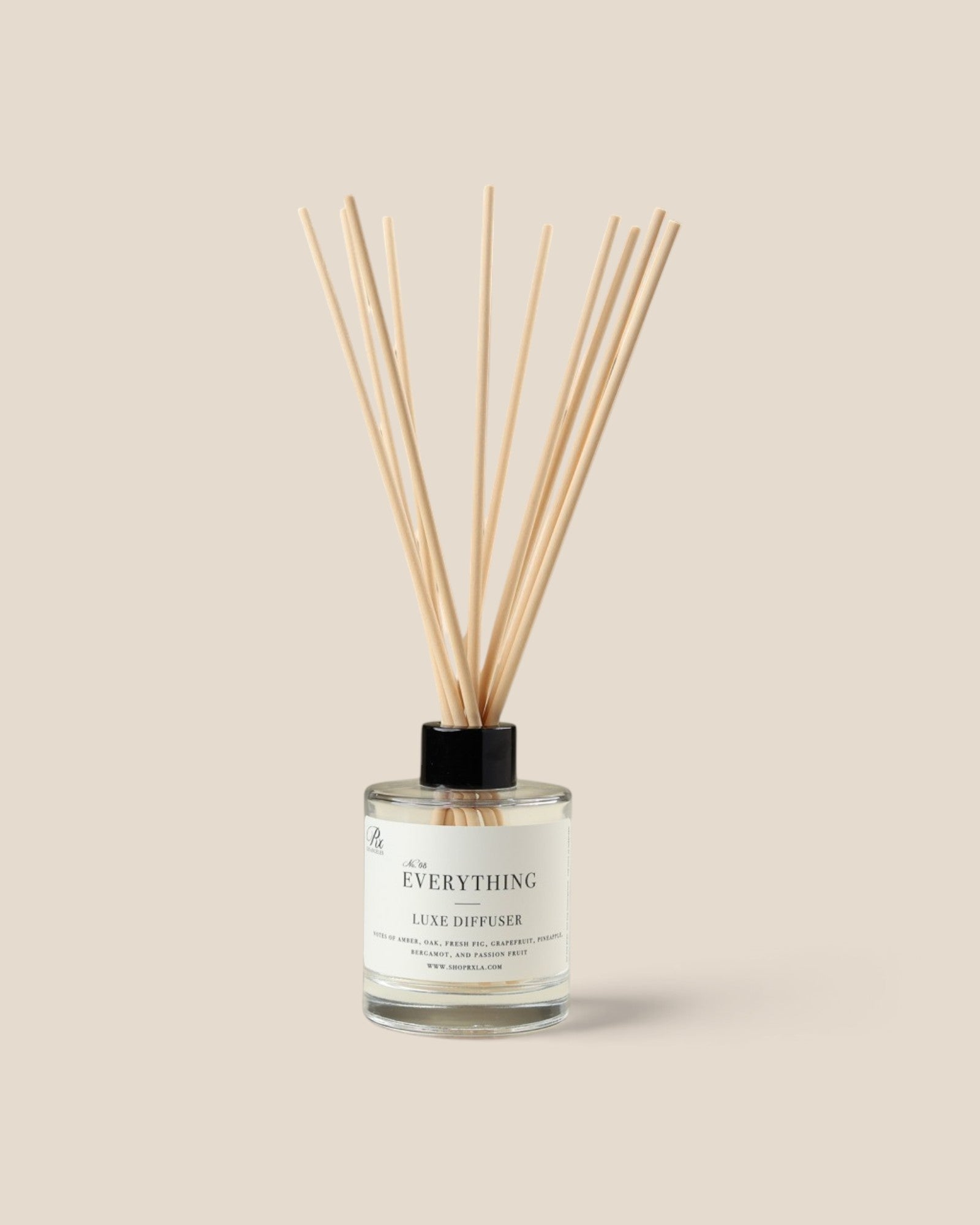 A reed diffuser bottle  filled with clear liquid and topped with fiber reeds, centered on a warm beige background.