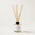 A reed diffuser bottle with a white label reading 'EARL GREY LUXE DIFFUSER' and natural wooden reeds extending upward, photographed on a clean off-white background.