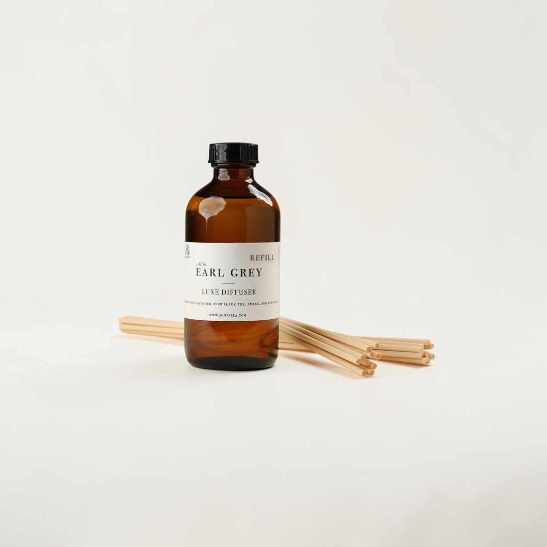 An amber glass reed diffuser bottle with a white label reading 'EARL GREY' and 'LEAVES DIFFUSER,' shown with several natural reed sticks on a clean white background.