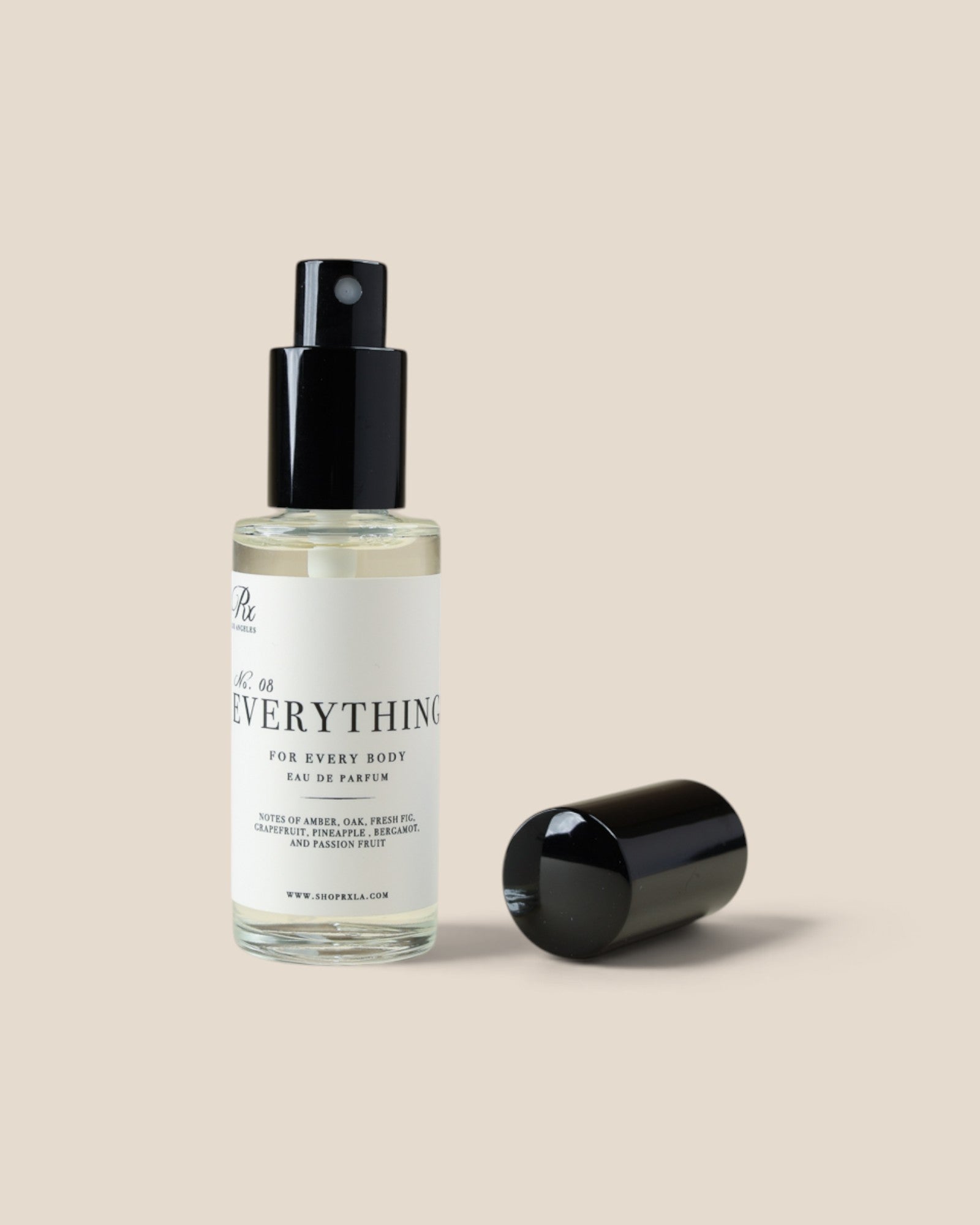 A clear glass spray bottle with a black pump dispenser and white label reading everything' on a warm beige background, with the black cap placed beside it.