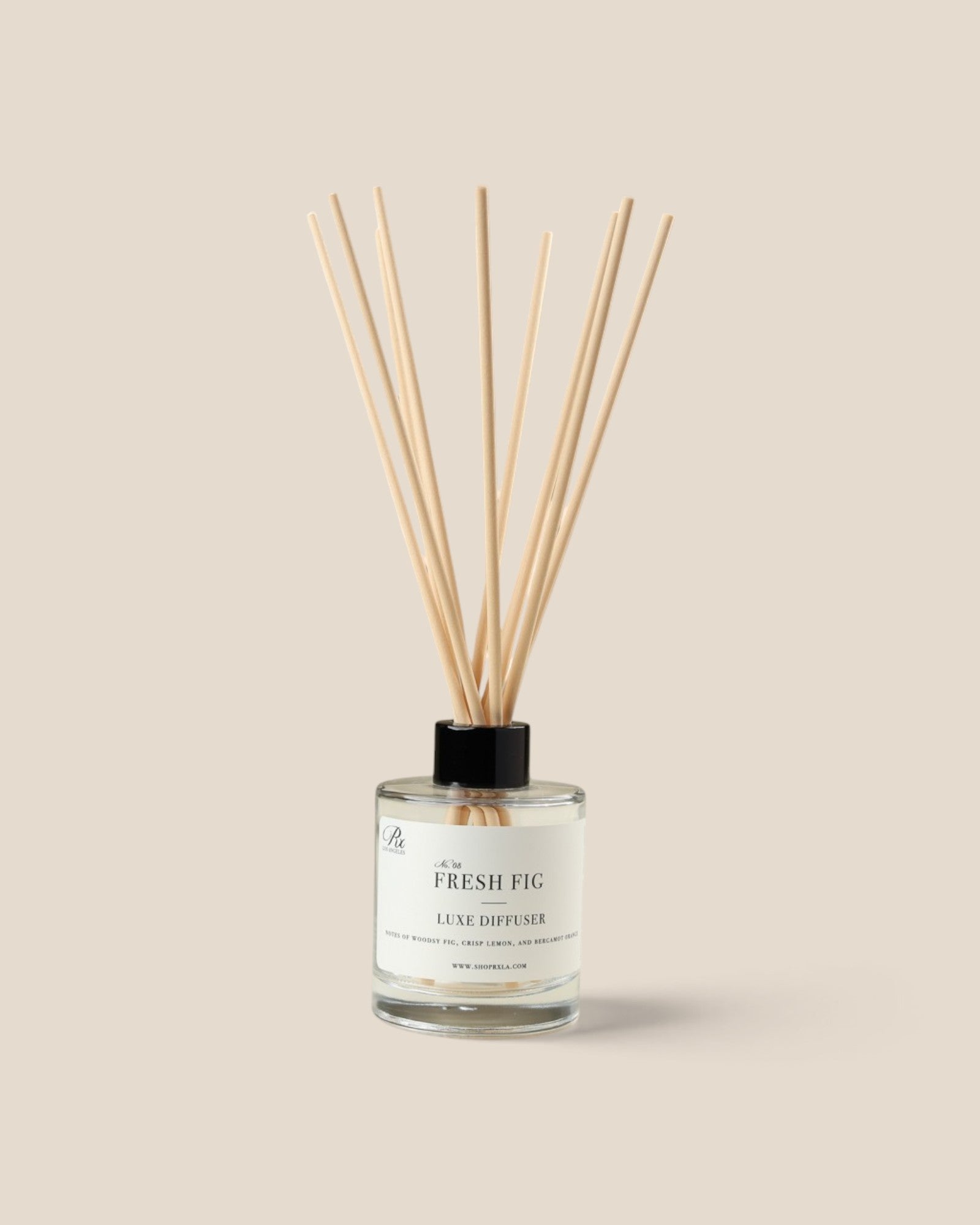 A reed diffuser bottle with a clear glass container, white liquid, a black cap, and diffuser reeds, labeled 'The Fresh Fig Local Diffuser', on a solid beige background.