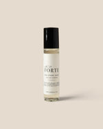 A clear cylindrical bottle of perfume with a black cap and a cream-colored label, centered on a solid beige background.