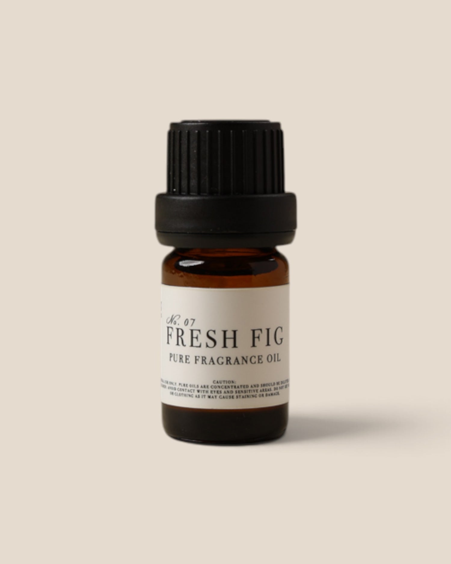 A small amber glass bottle of fragrance oil with a black ribbed cap and a cream label reading 'FRESH FIG PURE FRAGRANCE OIL', centered on a warm beige background.