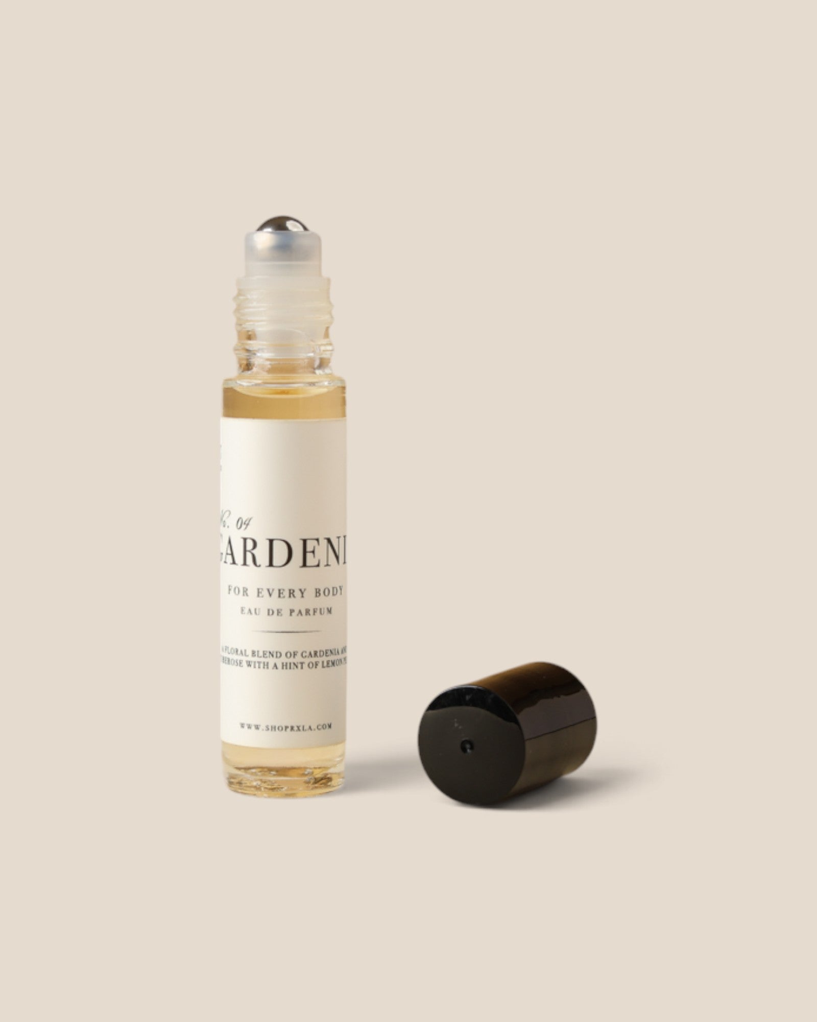A clear glass rollerball bottle with a cream label and black text, shown next to its detached black cap on a solid beige background. Gardenia label