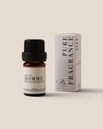 A bottle of Rc's Homme Pure Fragrance Oil next to its white box packaging, set against a solid beige background.