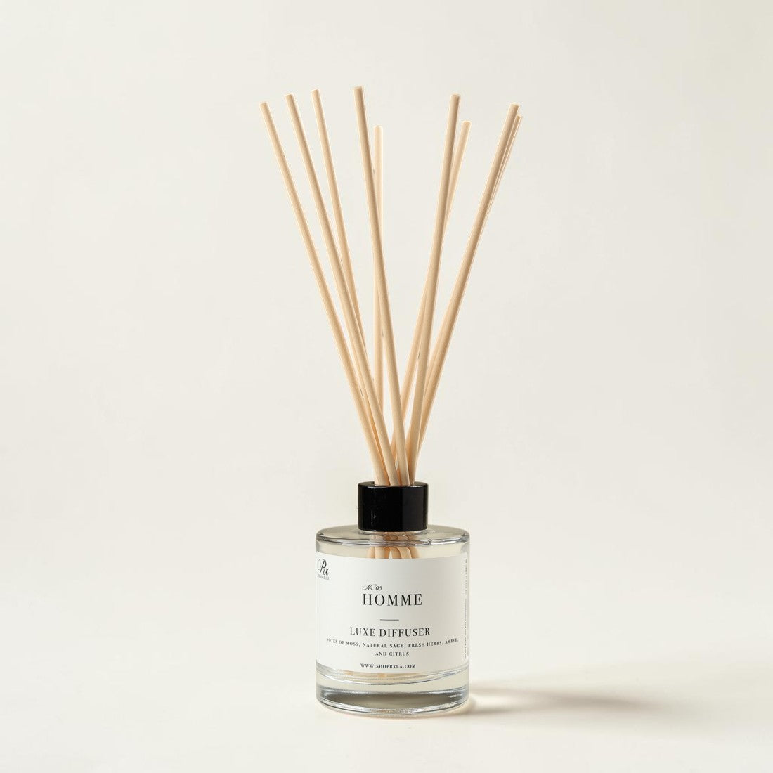 A reed diffuser bottle with a white label reading 'Le HOMME' and 'LUXE DIFFUSER', filled with clear liquid and topped with a black cap, with natural wood reeds extending upward against a plain light beige background.