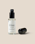 A clear glass bottle of HOMME  Eau de Parfum with a black spray pump, shown next to its detached black cap on a solid beige background.