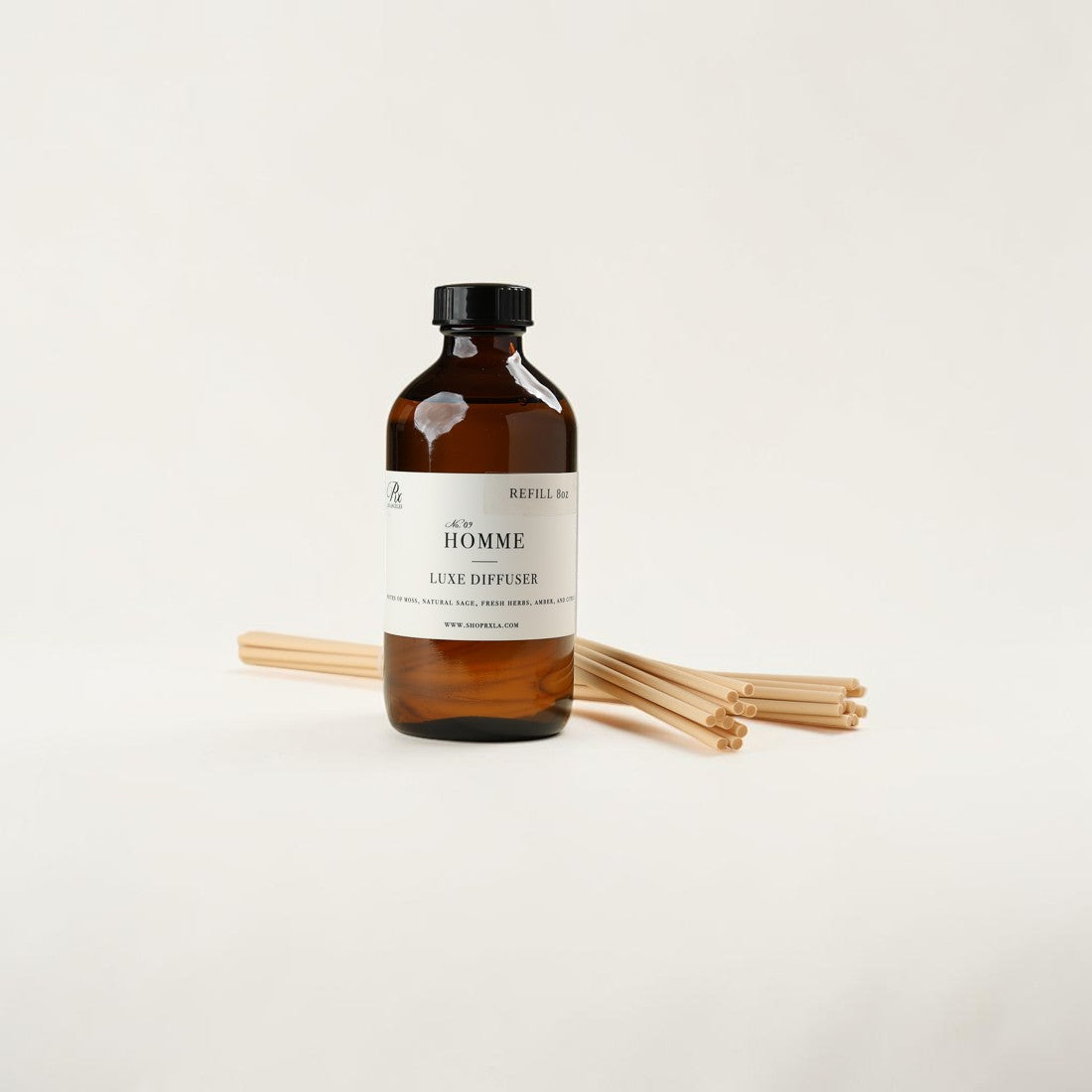 Amber glass bottle of REVEL No. 03 Élève Épiceux diffuser with a black cap and white label, shown with several natural wood diffuser sticks on a clean off-white background.