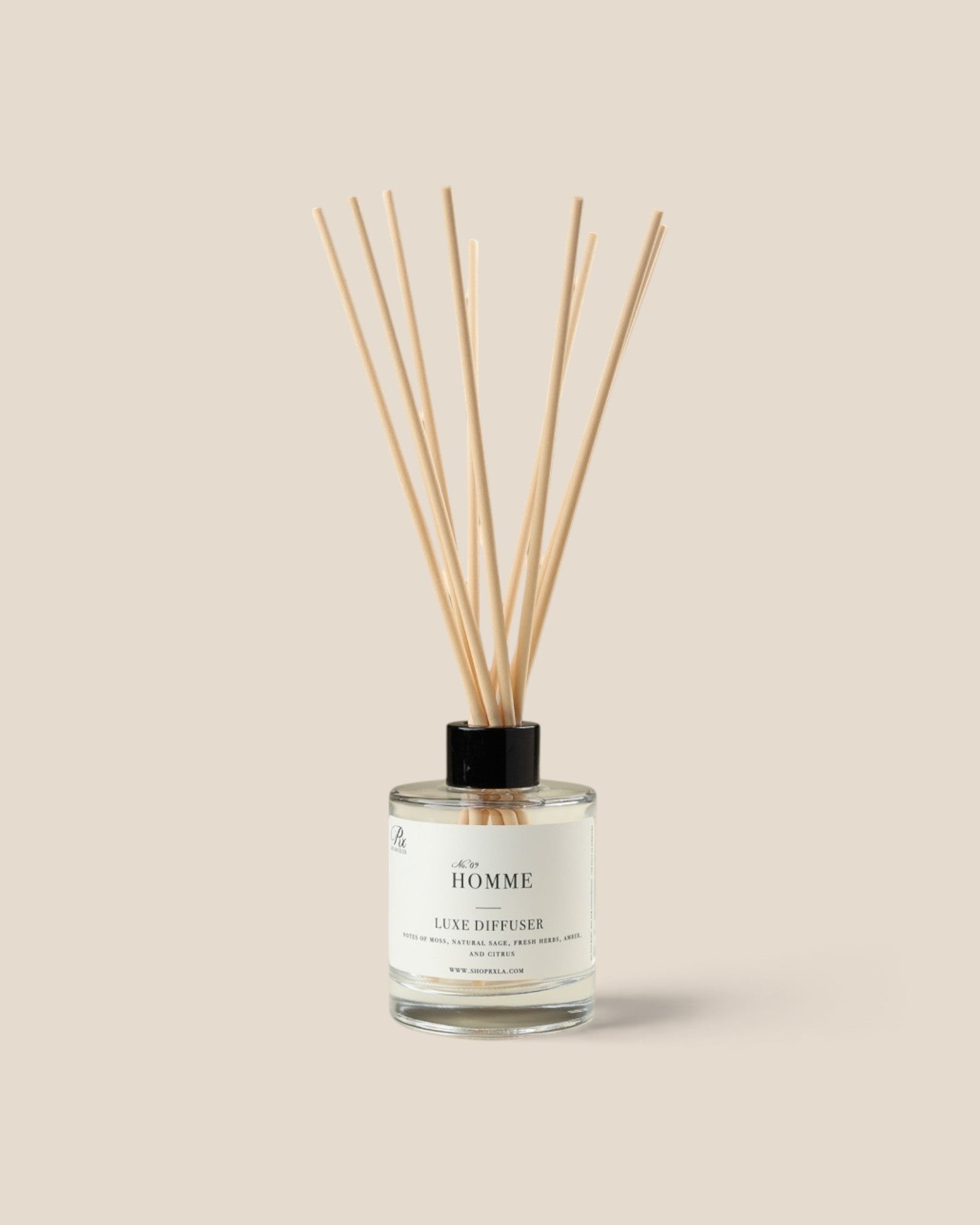 A reed diffuser bottle with a clear glass container, white label, black cap, and fiber reeds, centered on a warm beige background. The label reads 'Homme.