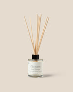 A Lake Tahoe Luxe Diffuser bottle with a clear glass body, white liquid, and fiber reeds, set against a solid beige background.