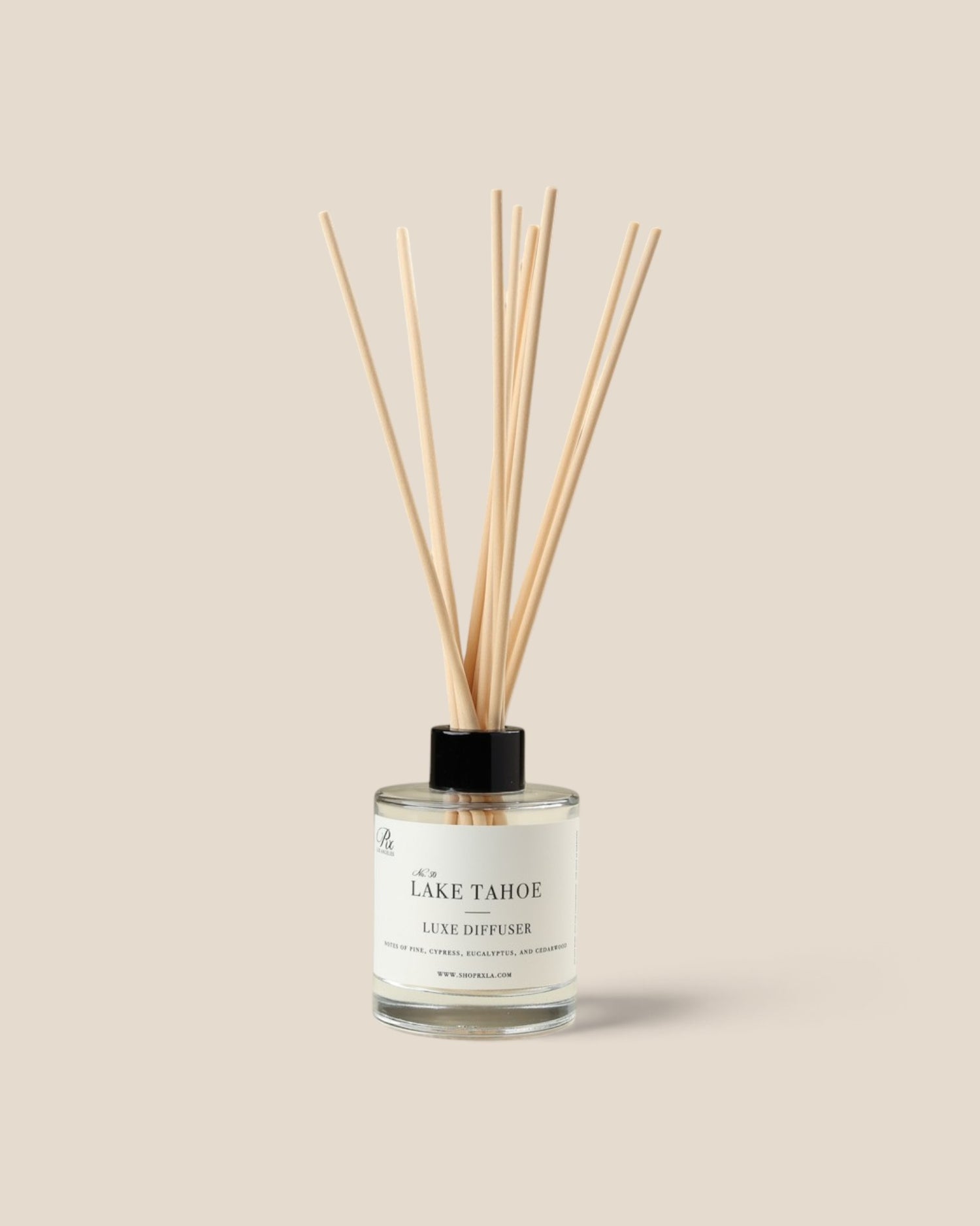 A Lake Tahoe Luxe Diffuser bottle with a clear glass body, white liquid, and fiber reeds, set against a solid beige background.