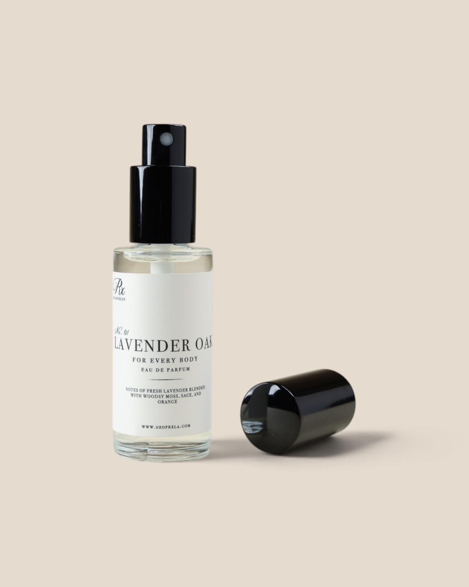 A clear glass spray bottle of Lavender Oil with a black pump dispenser and white label, shown next to its detached black cap on a solid beige background.