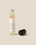 A clear glass rollerball bottle with a white label reading 'MANGO STICKY' and 'FOR EVERY BODY', shown with its black cap placed beside it on a warm beige background.
