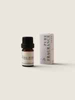 A small amber glass bottle with a black cap and a cream label reading 'BORA BORA PURE FRAGRANCE OIL' stands next to its matching cream-colored box on a warm off-white background.