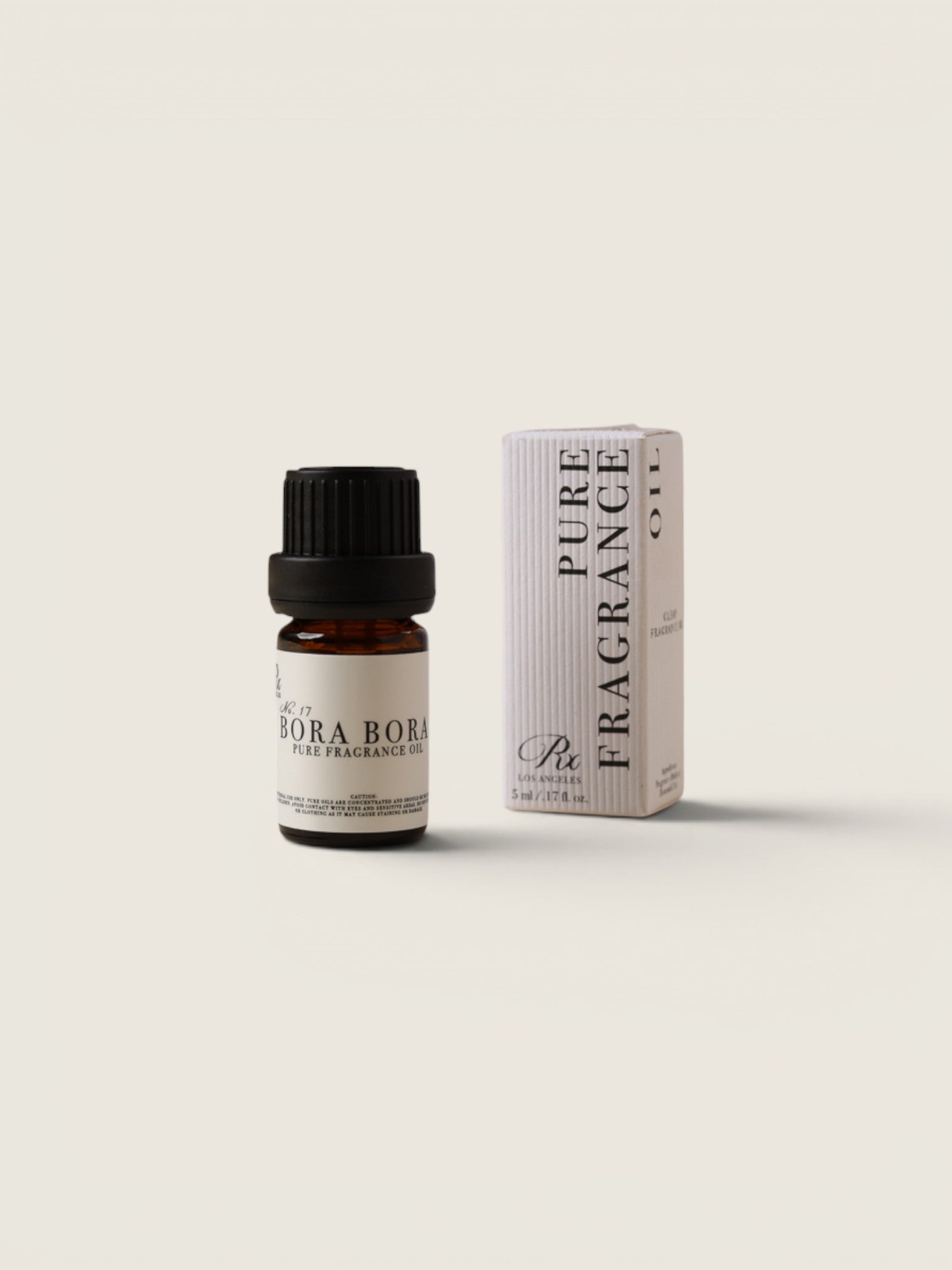 A small amber glass bottle with a black cap and a cream label reading 'BORA BORA PURE FRAGRANCE OIL' stands next to its matching cream-colored box on a warm off-white background.