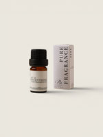 A small amber glass bottle of fragrance oil with a black cap stands next to its white and pale pink box. The label reads 'No.