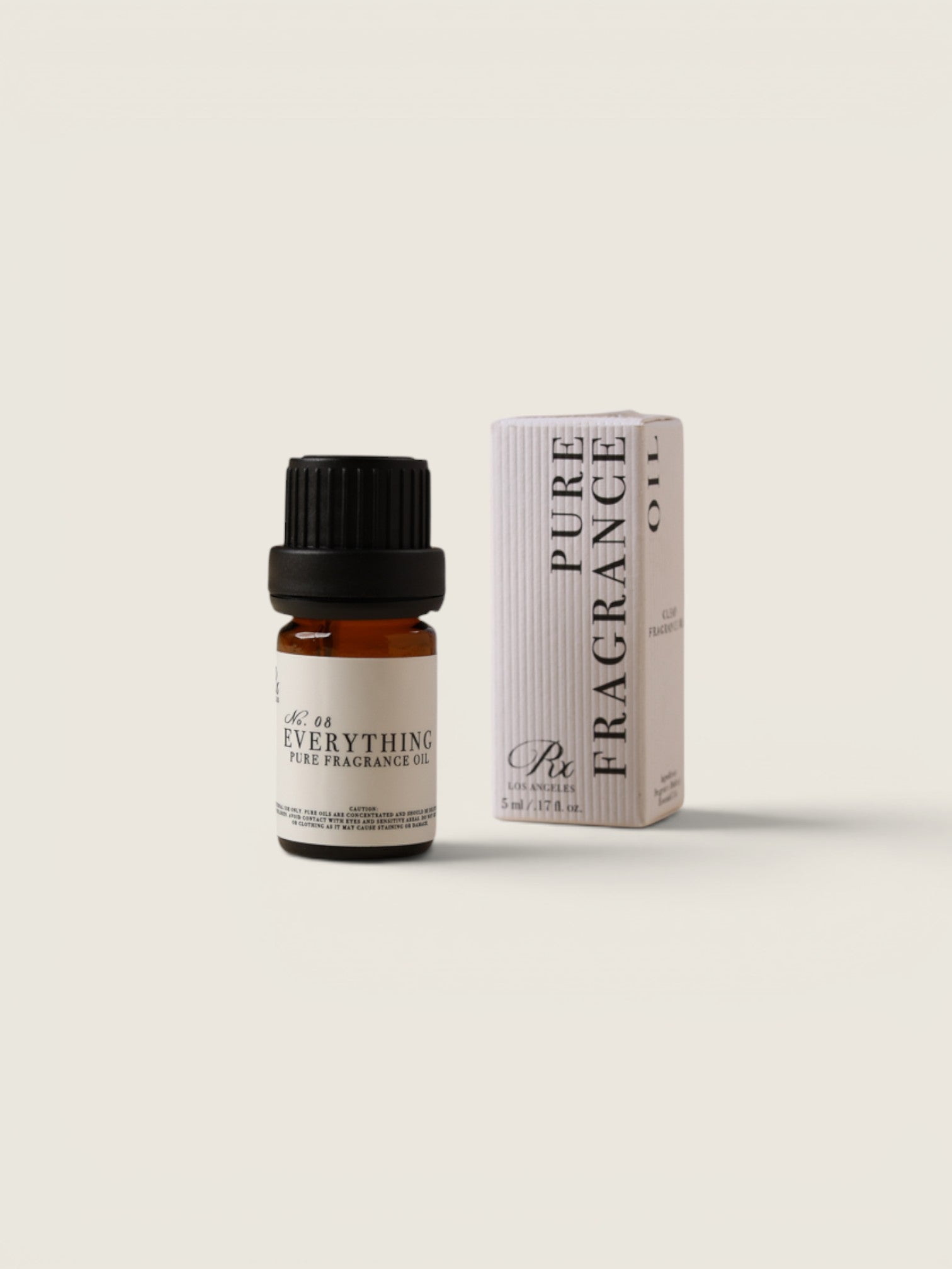 A small amber glass bottle of fragrance oil with a black cap stands next to its white and pale pink box. The label reads 'No.