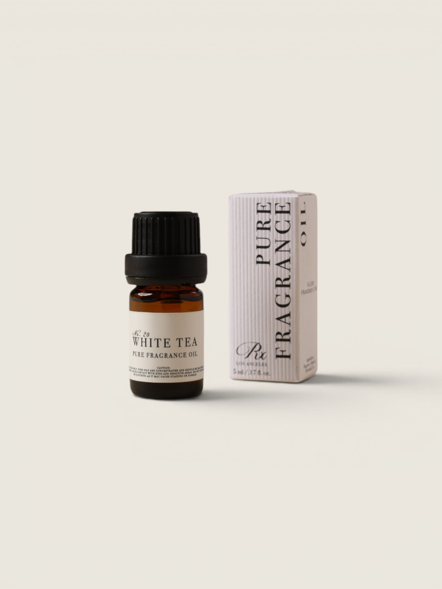 A small amber glass bottle of white tea pure fragrance oil with a black cap stands next to its white and black packaging box on a light beige background.