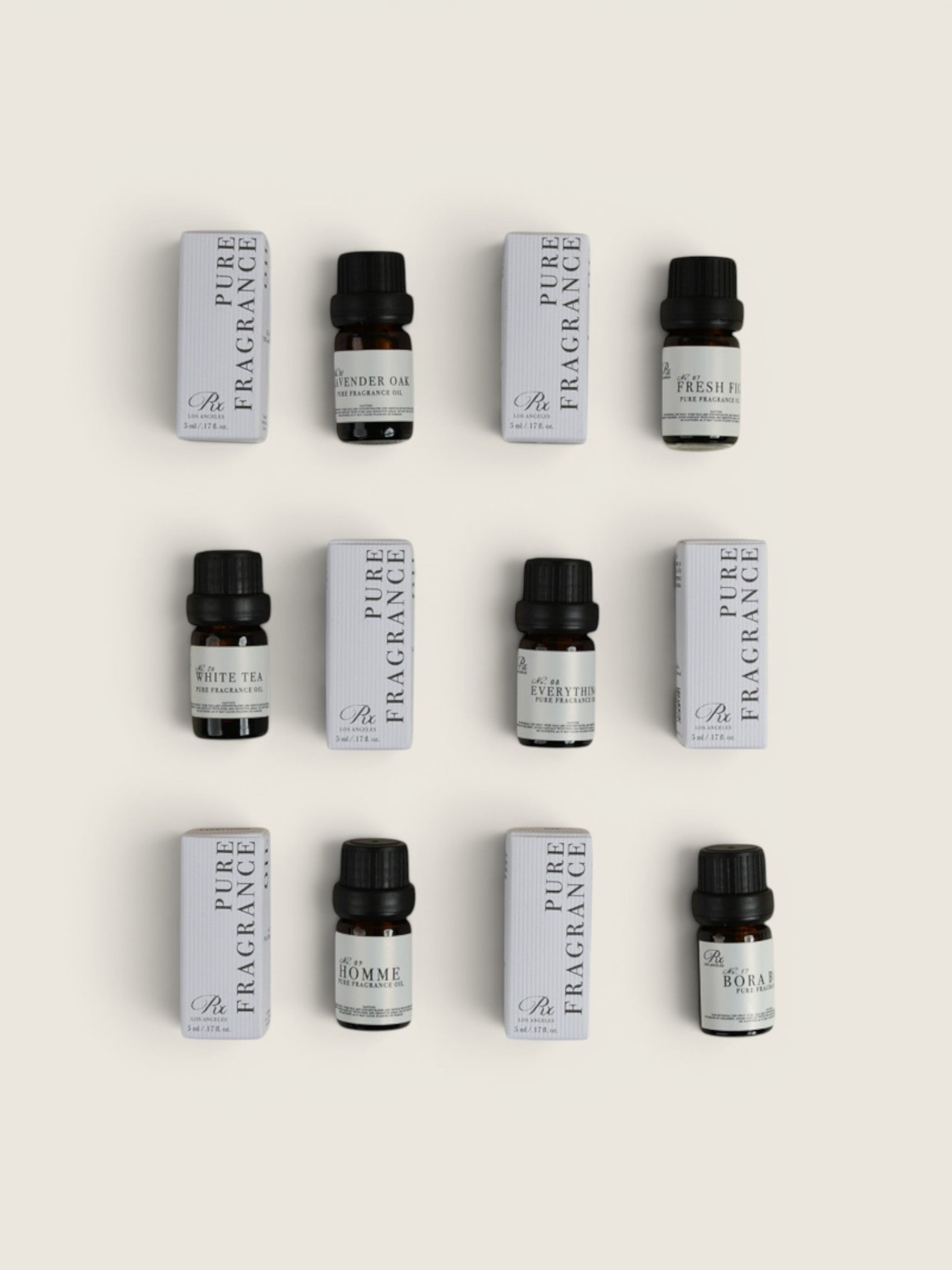 Nine small fragrance bottles with black caps arranged in a 3-by-3 grid alongside matching white rectangular boxes on a light beige background. The labels show Pure Fragrance oil