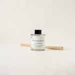 A South Hampton Luxe Diffuser bottle with a black cap and clear glass, shown with four natural wood reeds on a clean off-white background.