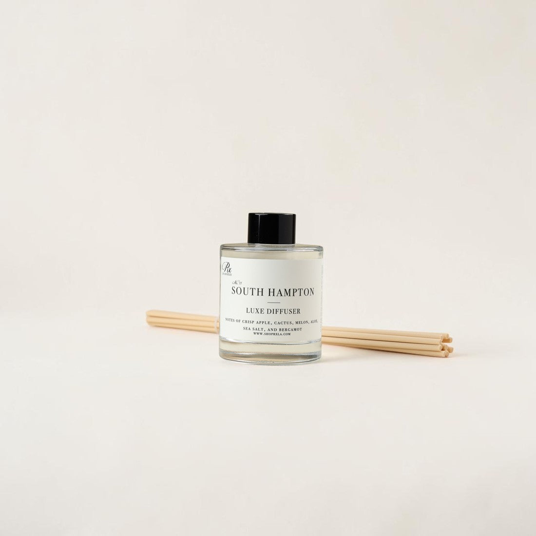 A South Hampton Luxe Diffuser bottle with a black cap and clear glass, shown with four natural wood reeds on a clean off-white background.