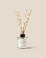 A glass reed diffuser bottle with a black cap and natural wood reeds, labeled 'A SOUTH HAMPTON LUXE DIFFUSER', centered on a solid beige background.
