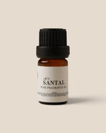 A small amber glass bottle of Santal Pure Fragrance Oil with a black ribbed cap and a white label, centered on a solid beige background.