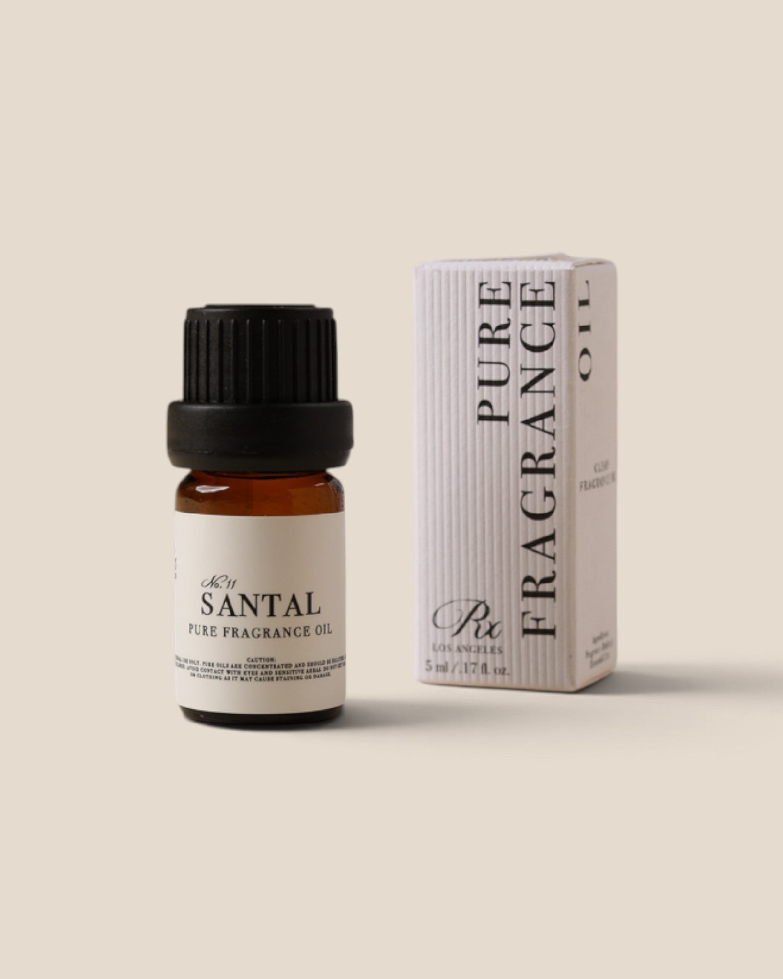 A small amber glass bottle of pure fragrance oil with a black cap stands next to its white box packaging on a solid beige background. The label reads 'Santal Pure Fragrance Oil' and the box reads 'PURE FRAGRANCE OIL' with 'Ric' branding.