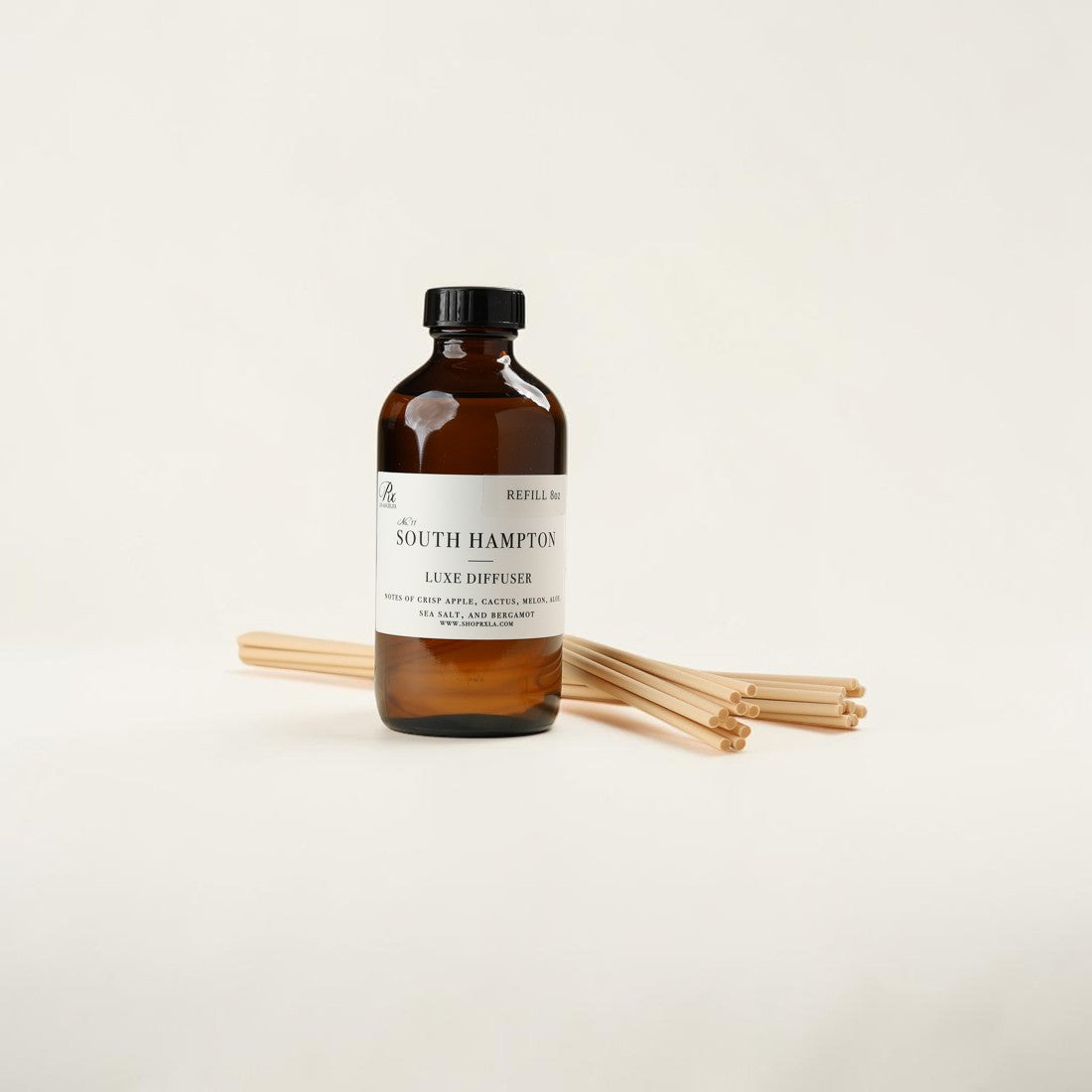 An amber glass bottle of South Hampton Luxe Diffuser with a black cap and white label, standing upright with several natural wood diffuser sticks behind it on a clean off-white background.