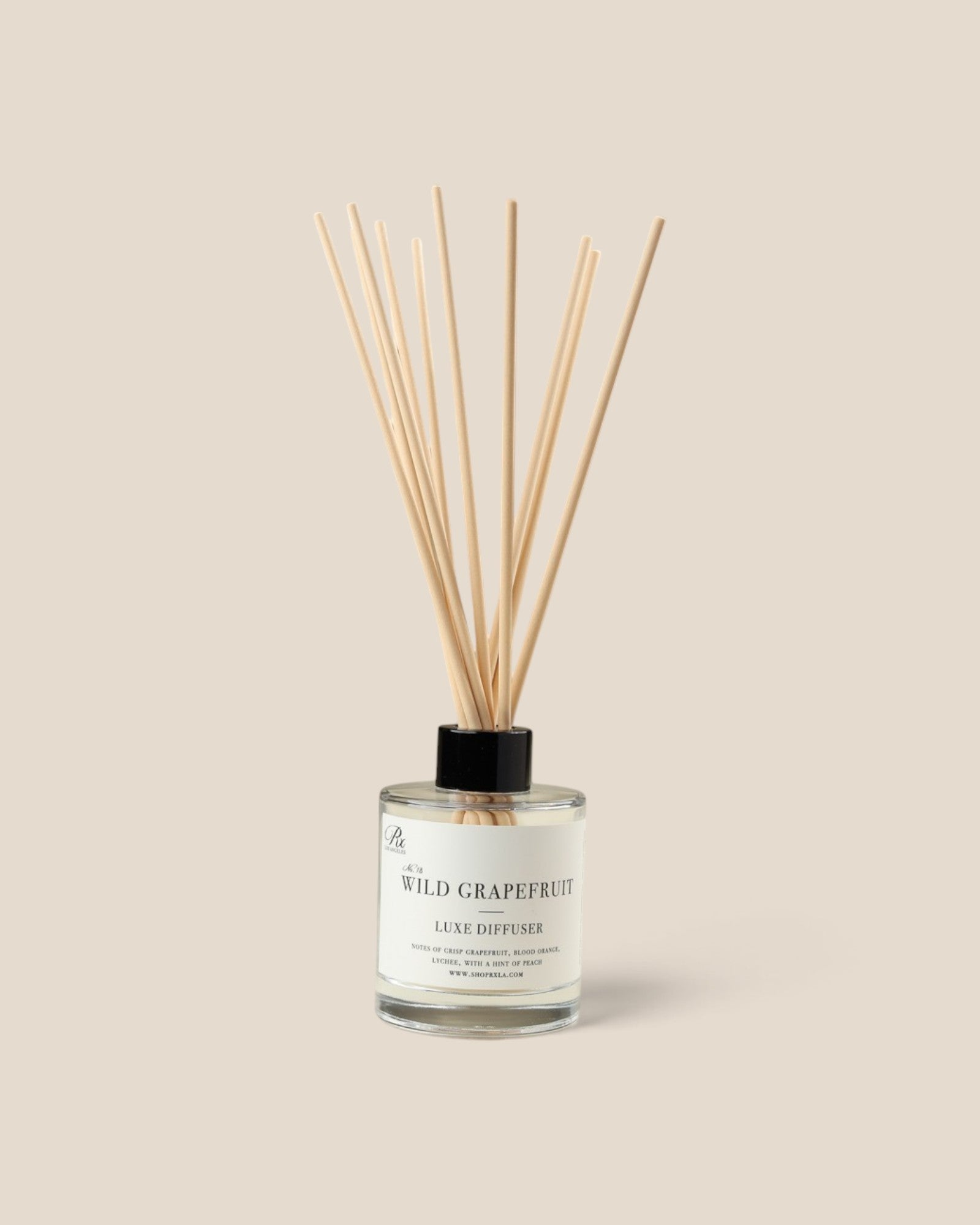 A reed diffuser bottle with natural wooden reeds, a clear glass container, and a black cap, labeled 'The Wild Grapefruit' by 'RXLA', set against a solid beige background.