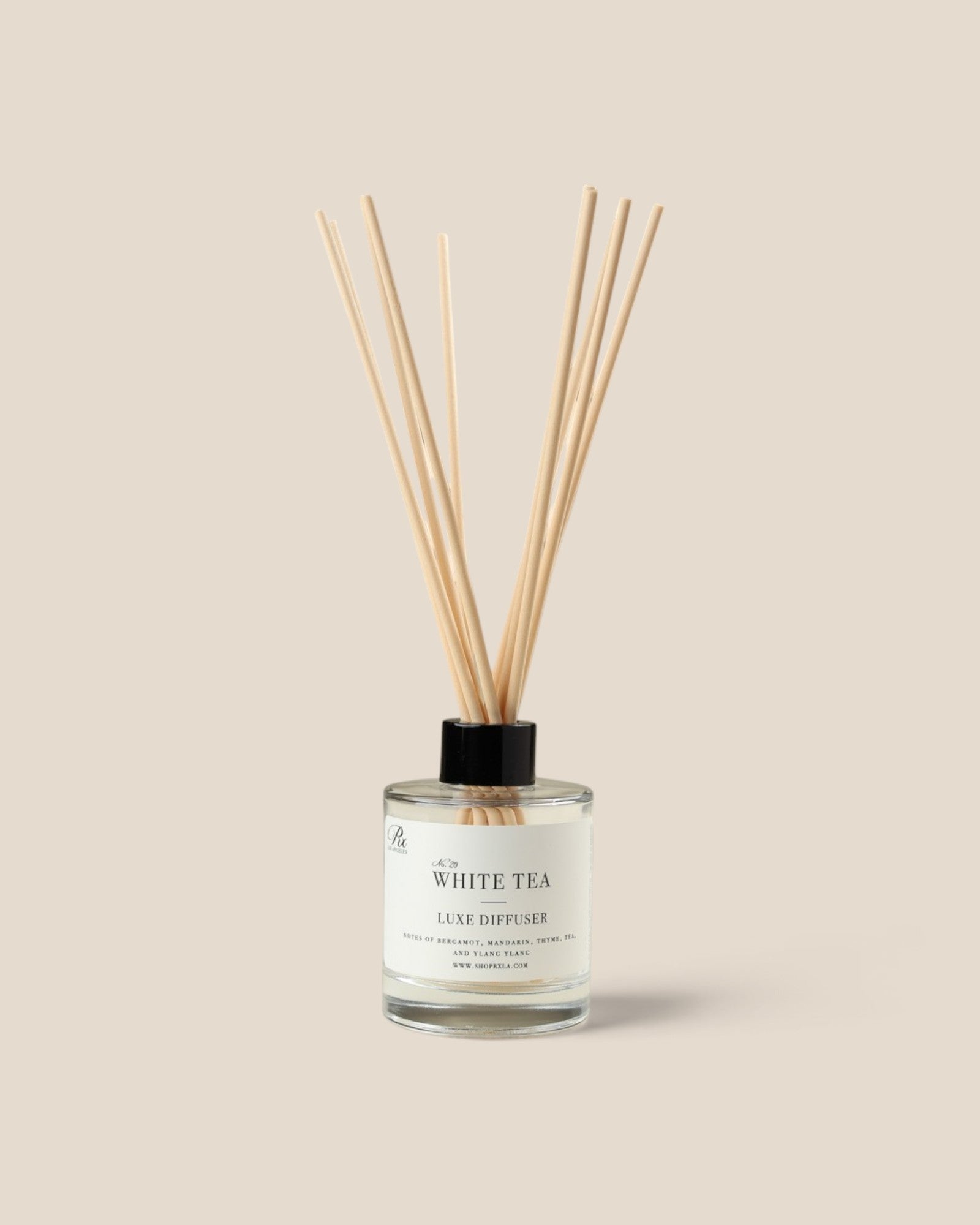 A reed diffuser bottle with a clear glass body, white label reading 'WHITE TEA', and fiber reeds extending upward against a plain warm beige background.