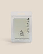 A packaged wax melt in a clear plastic clamshell package with a white backing card. The label reads 'WAX MELTS' vertically and 'EARL GREY' below a small line drawing of a melting pot, on a warm beige background.