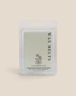 A wax melt package labeled 'WAX MELTS' and 'LAVENDER OAK' in a clear plastic clamshell with a white backing card, centered on a warm beige background.
