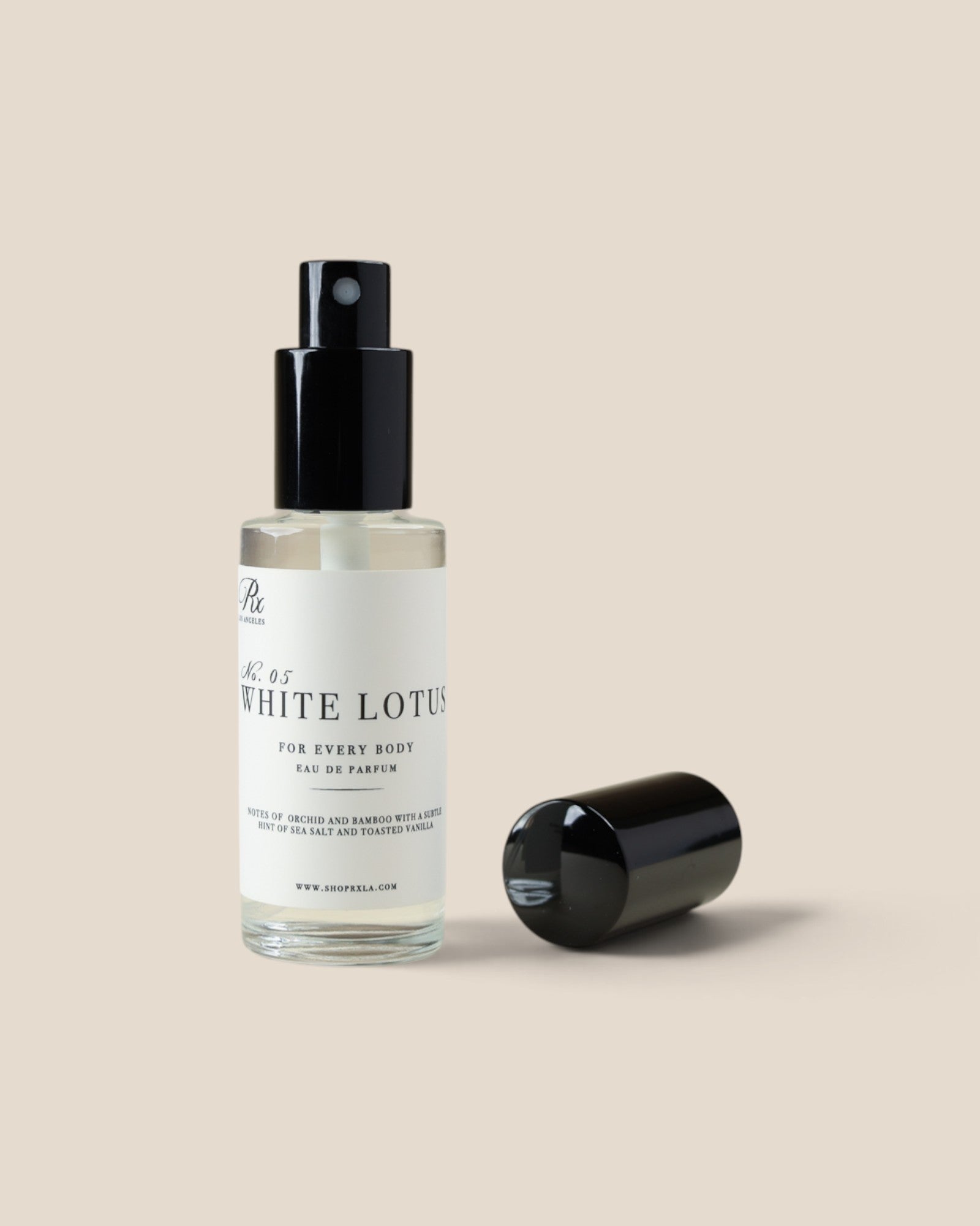 A clear glass spray bottle labeled 'whit lotus' with a black pump and a separate black cap, shown on a plain warm beige background.