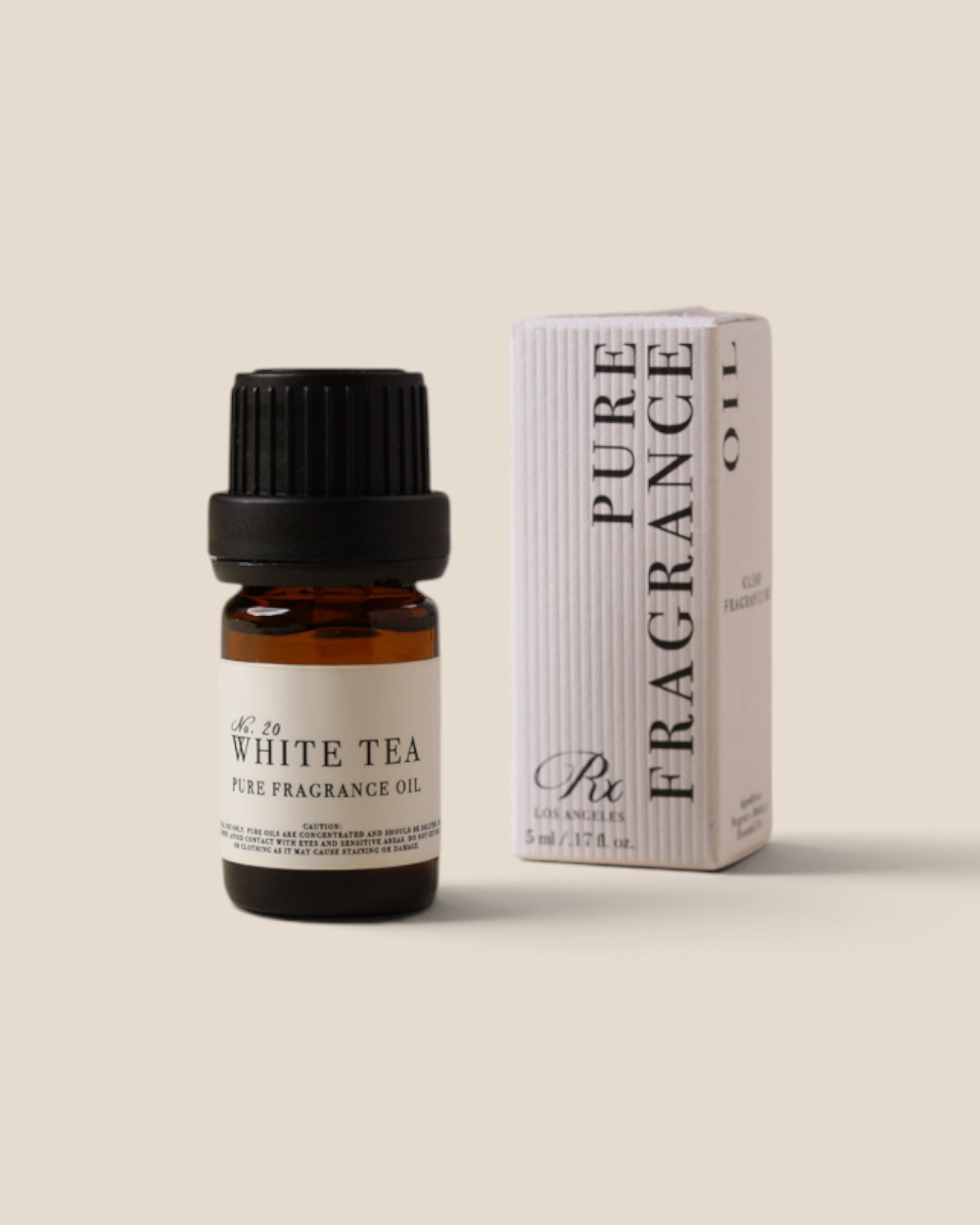 A small amber glass bottle of White Tea Pure Fragrance Oil with a black cap stands next to its white ribbed packaging box on a warm beige background.