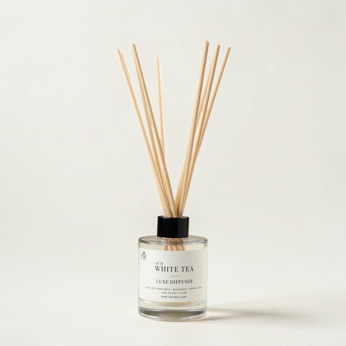 A reed diffuser bottle with a clear glass base, white label reading 'White Tea Luxe Diffuser,' and natural wood reeds extending upward against a clean off-white background.