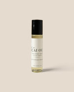 A small cylindrical rollerball bottle of Aqai Oud fragrance oil with a black cap and a white label, set against a solid beige background.